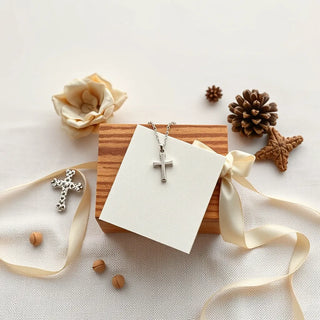Silver cross pendant and keepsake box with a ribbon and prayer card on a neutral tabletop