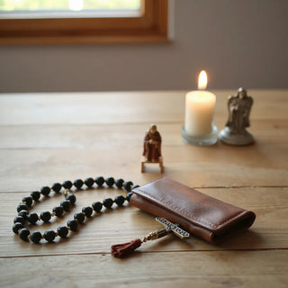 Rosary, small devotional icon, and a lit candle arranged on a wooden table for prayer