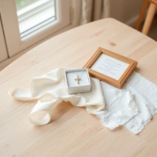 Baptism keepsake items including a cross pendant, prayer card, and ribbon on a light wood table